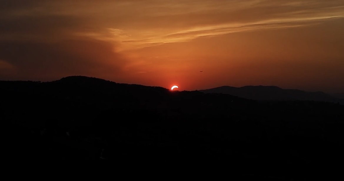 Sun setting over silhouetted hills under an orange sky.