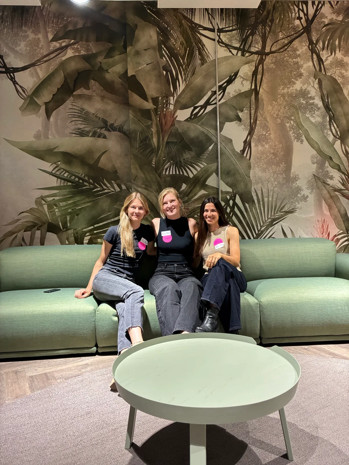 The three Women in AI Social co-hosts sitting together on a green couch.