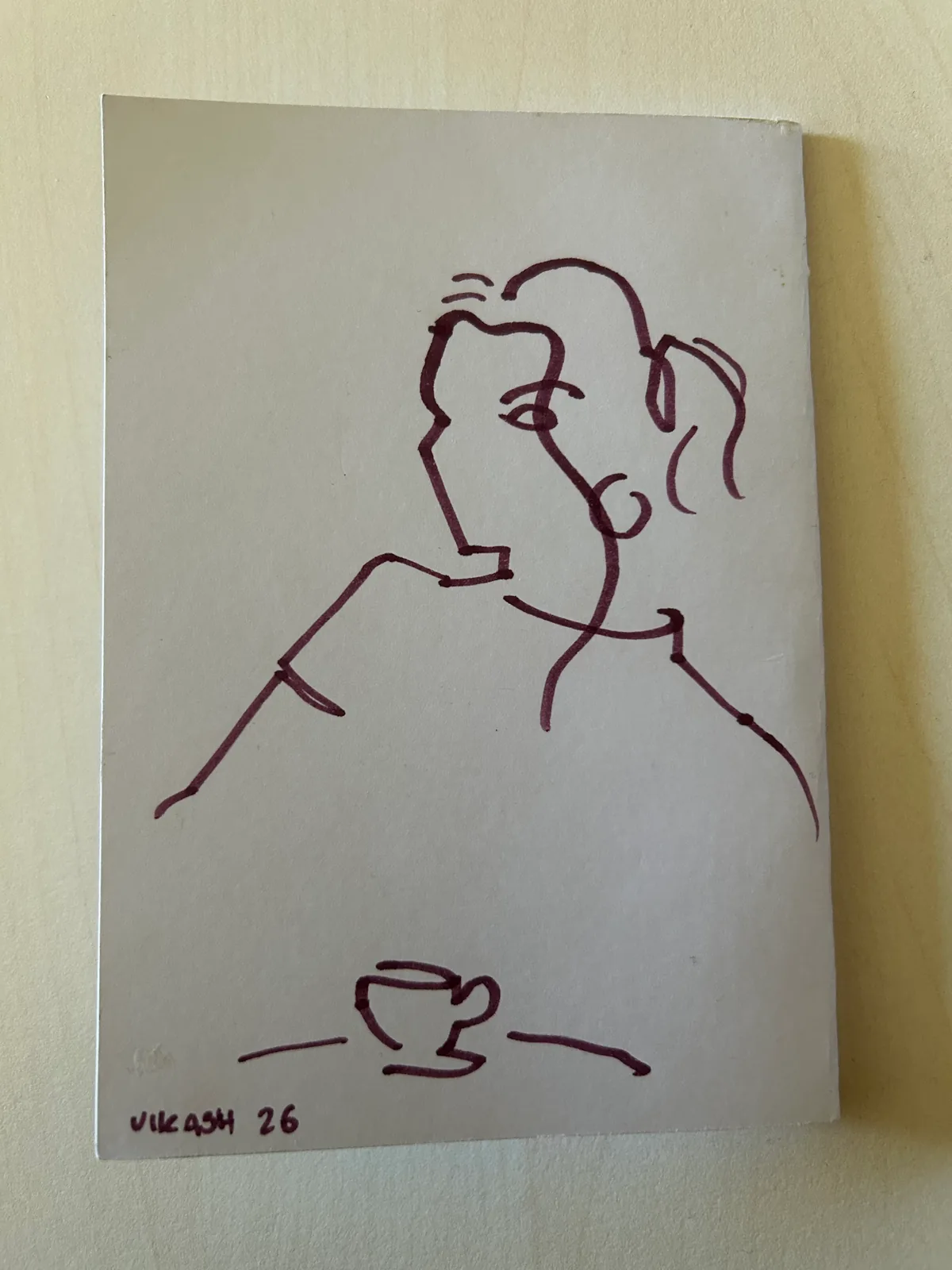 Vikash’s original burgundy line drawing of Lara with a coffee cup, signed Vikash 26.