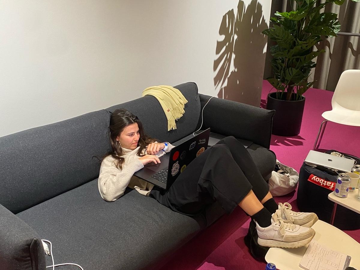 Lara coding from a couch with notebooks and drinks around her.